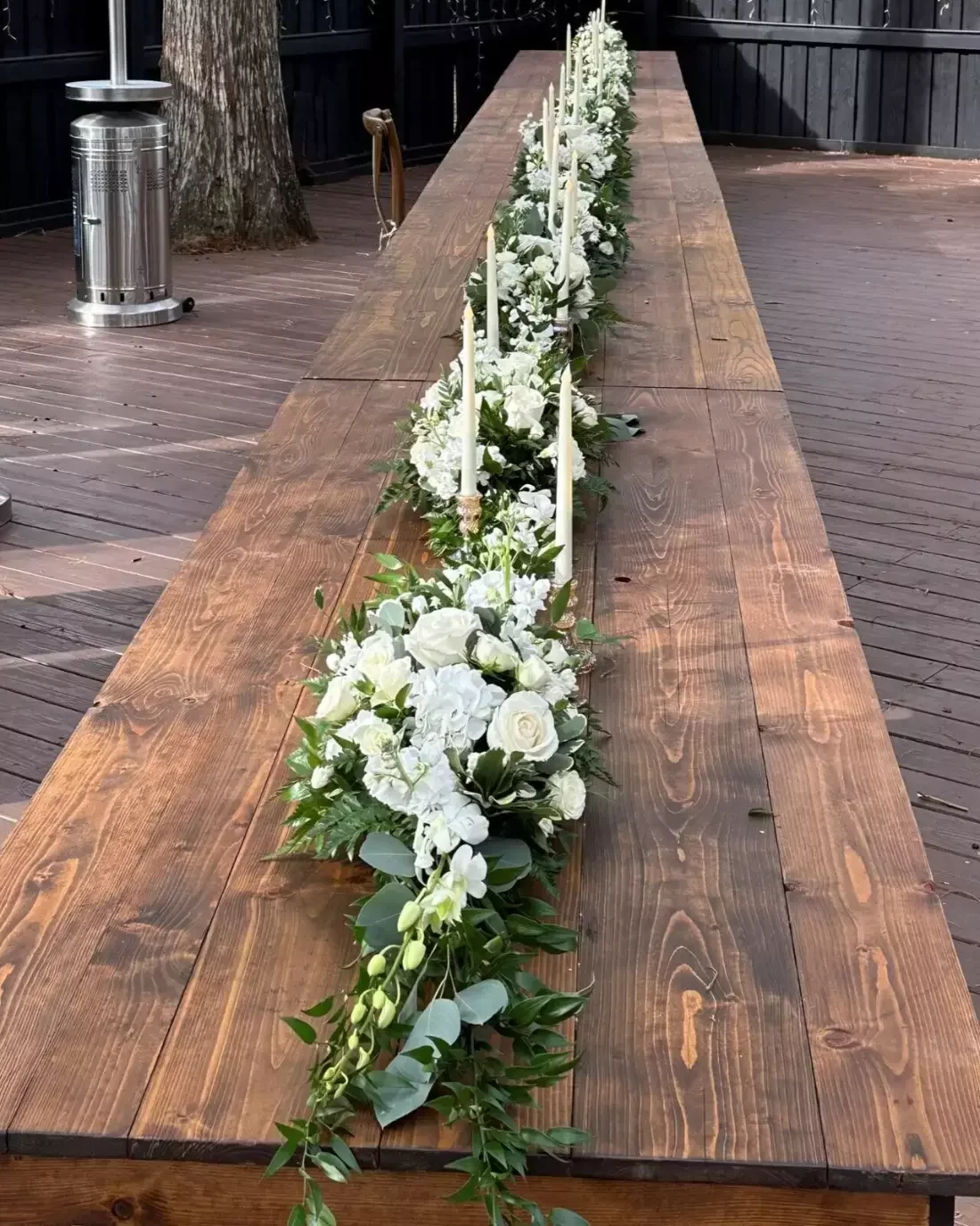 White floral and greenery garland running down a long farm table at an outdoor wedding reception