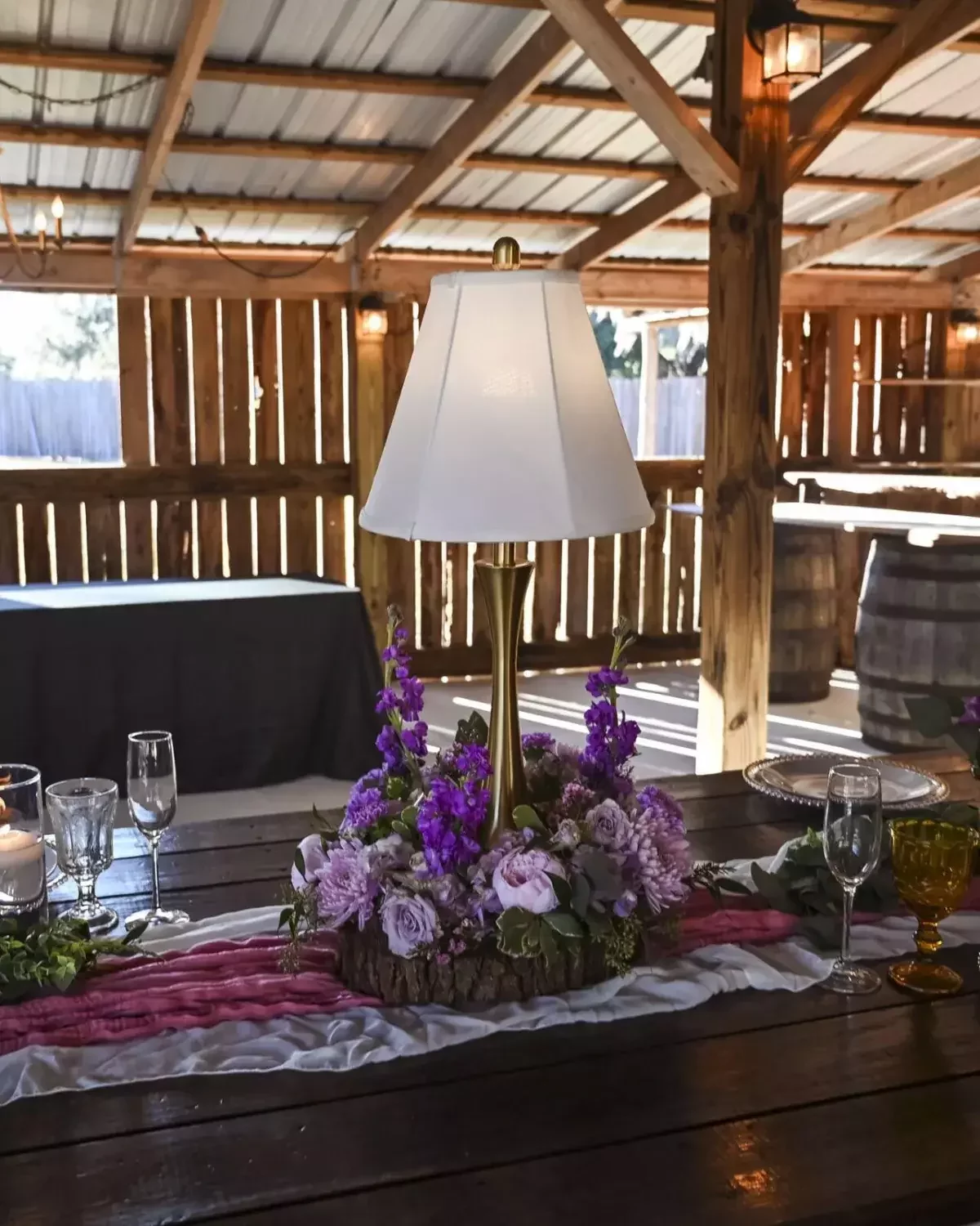 Lamp centerpiece with purple and lavender flowers on a rustic barn wedding reception table