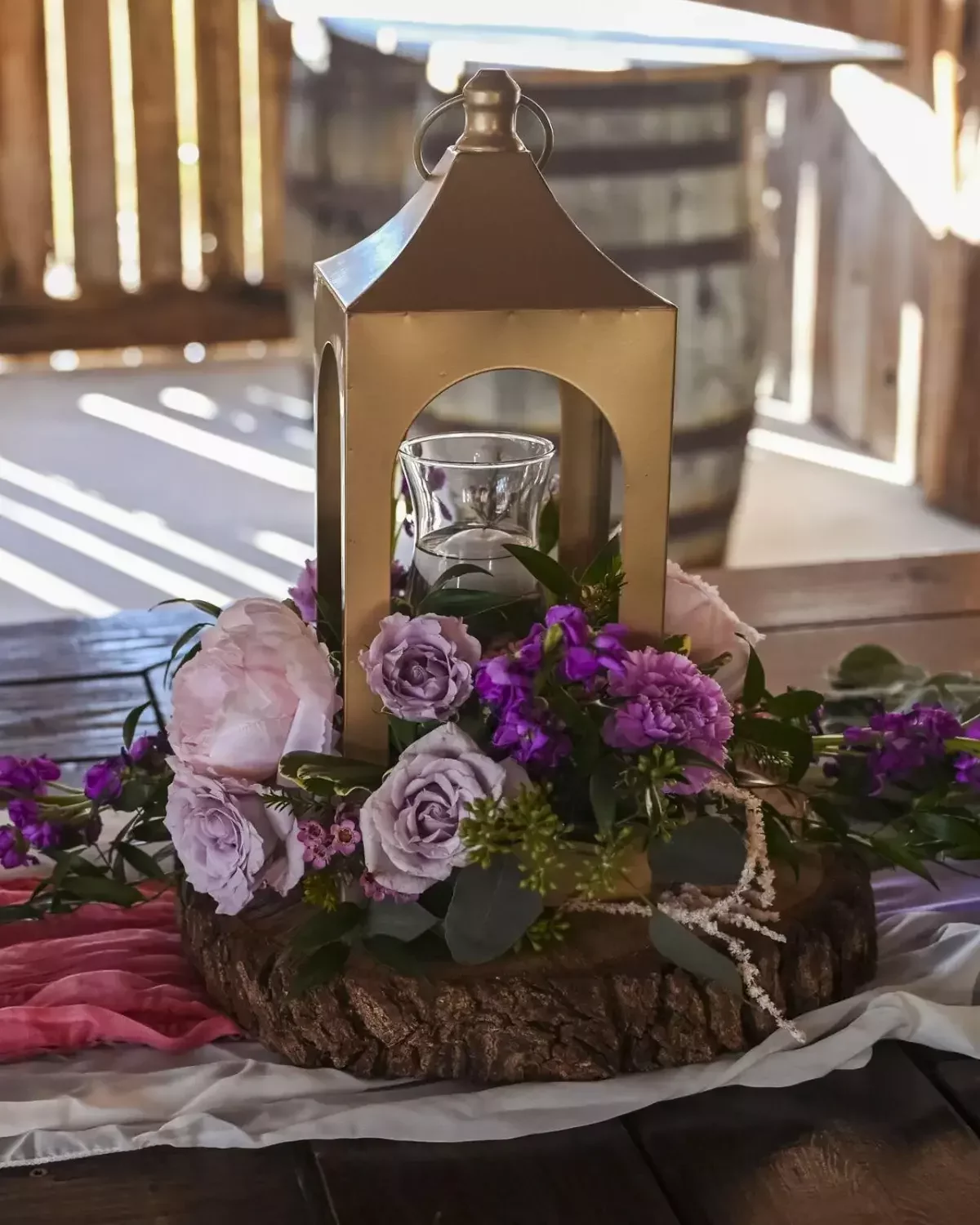 Gold lantern wedding centerpiece surrounded by purple and lavender roses on a wood slab