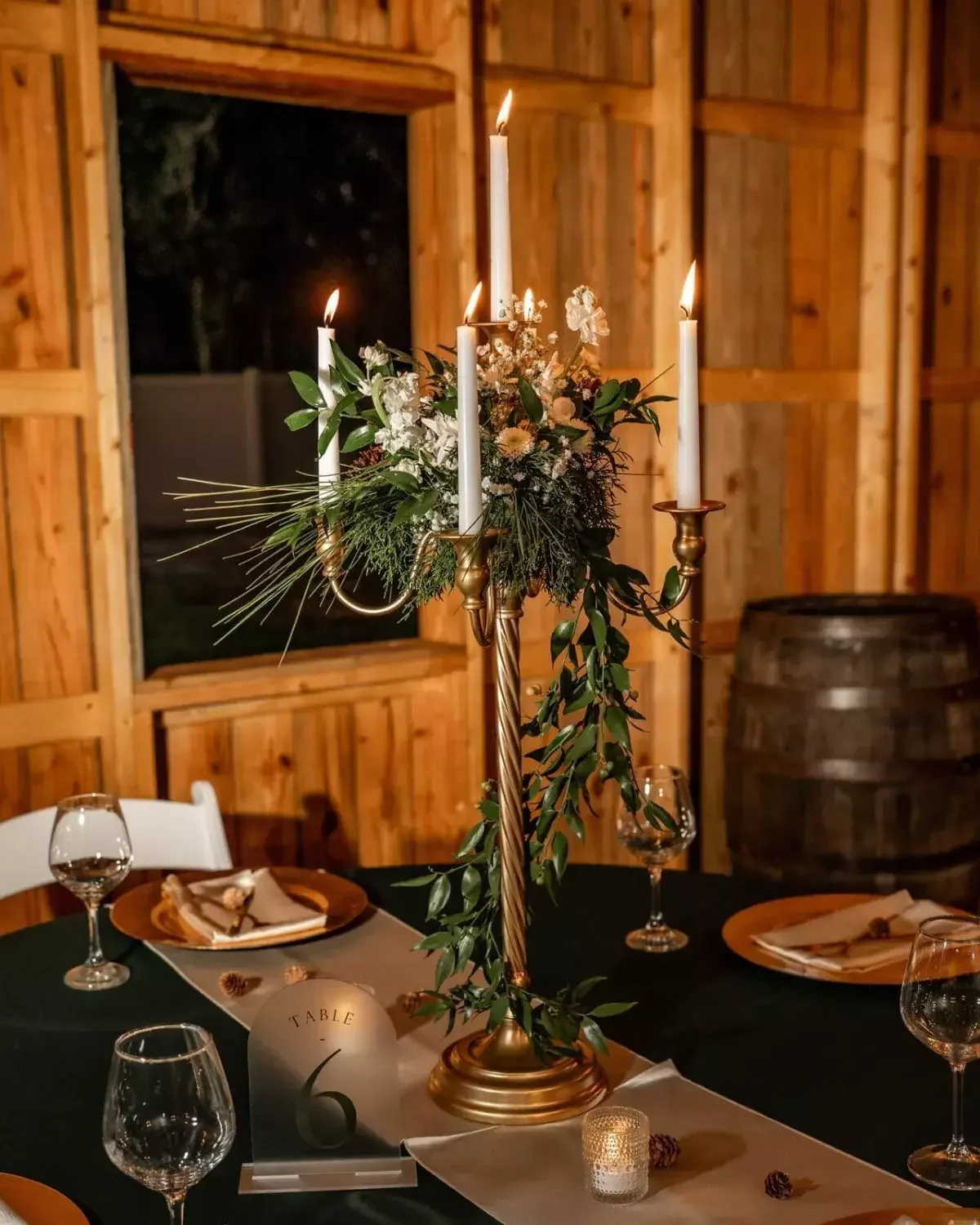 Gold candelabra wedding centerpiece with taper candles and greenery on a rustic reception table