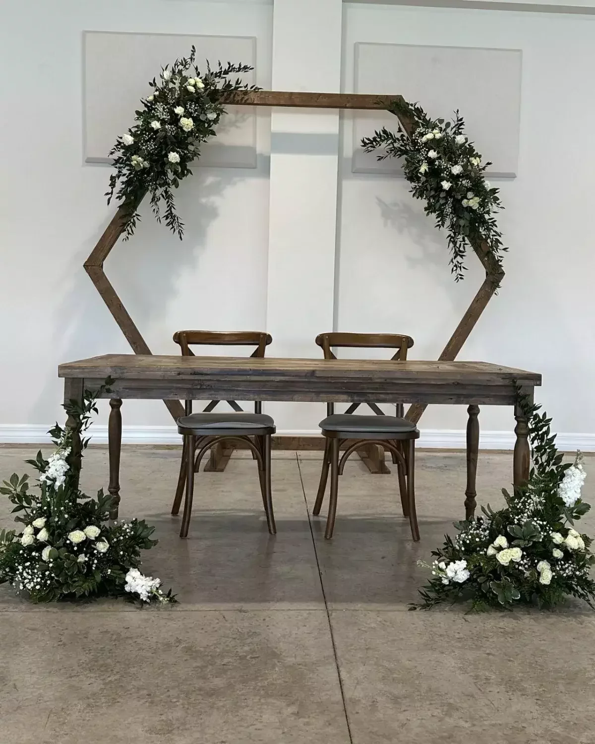 Hexagon arch with white flowers and greenery framing a rustic wedding sweetheart table