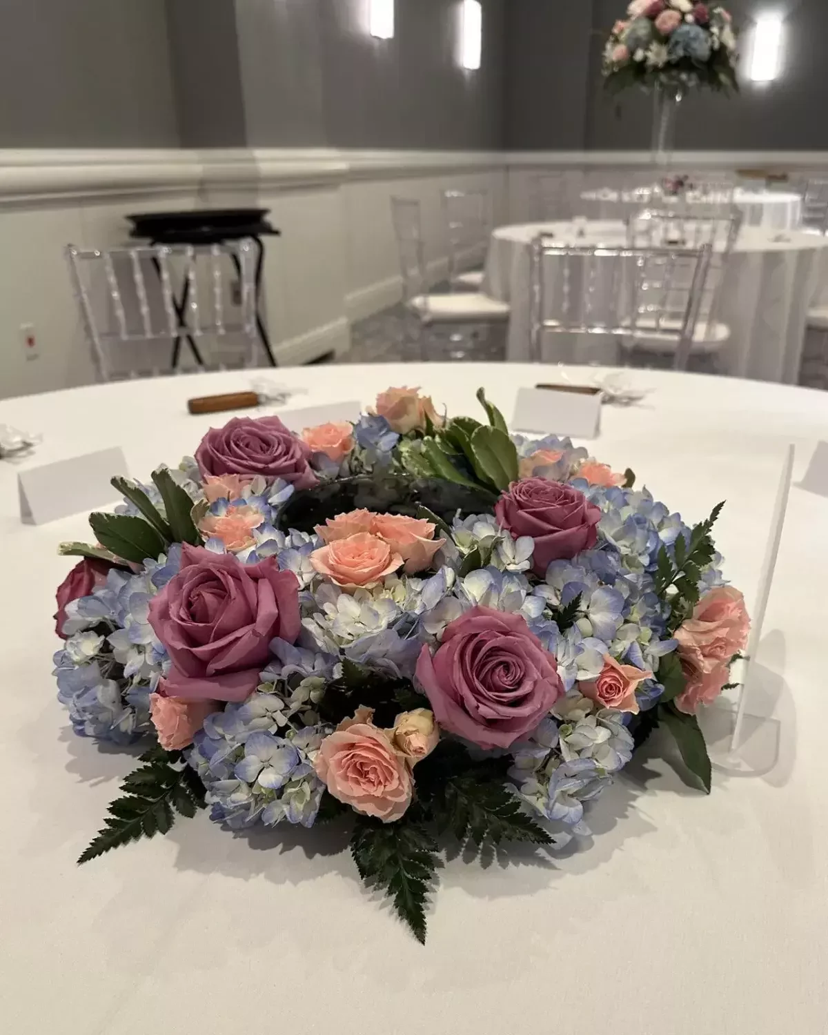 Low wedding centerpiece of mauve roses, peach roses and blue hydrangea at a Tampa Bay reception